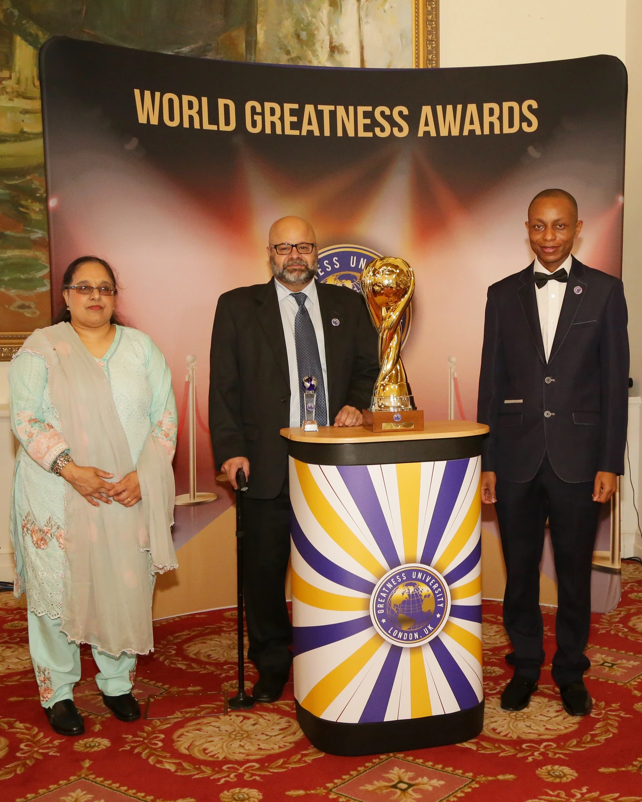 Three attendees beside trophies at a World Greatness Awards event